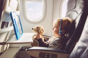 child sitting in plane with headphones and plush toy